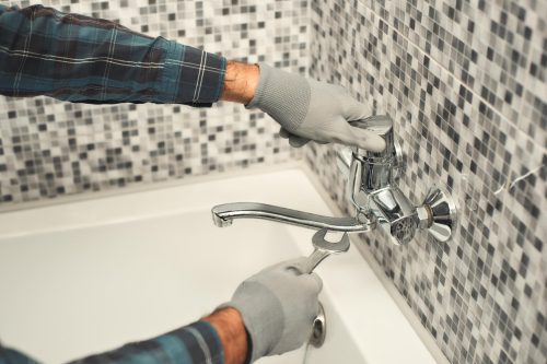 Close up of male hands holding a wrench, while fixing faucet in bathroom. Horizontal shot